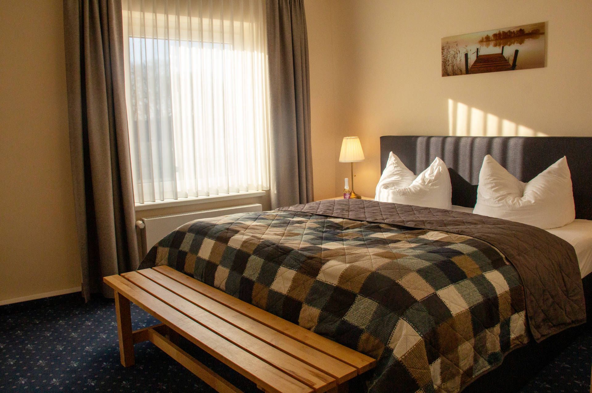 Une chambre d’hôtel avec un lit, une banquette, une table de chevet avec une lampe et un tableau au mur.