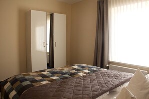 A bedroom with a bed, a wardrobe, a window with curtains, and a radiator. - Am Wiesenblick - Müritz apartment (Röbel/Müritz)