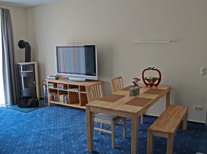 A hotel room with a wooden dining table, a television, a bookshelf, and a fireplace.