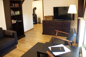 A living room with a sofa, a table with a book, a TV, and a bookshelf. - Holiday ivy - Müritz apartment (Röbel/Müritz)