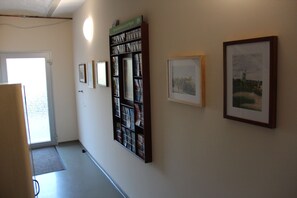 A hallway with framed pictures on the wall, a bookshelf, and a door leading outside.