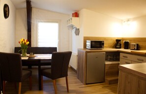 A compact kitchen with a microwave, toaster, and coffee maker. There is a dining area with chairs and a table, and a small refrigerator. - Holiday ivy - Müritz apartment (Röbel/Müritz)