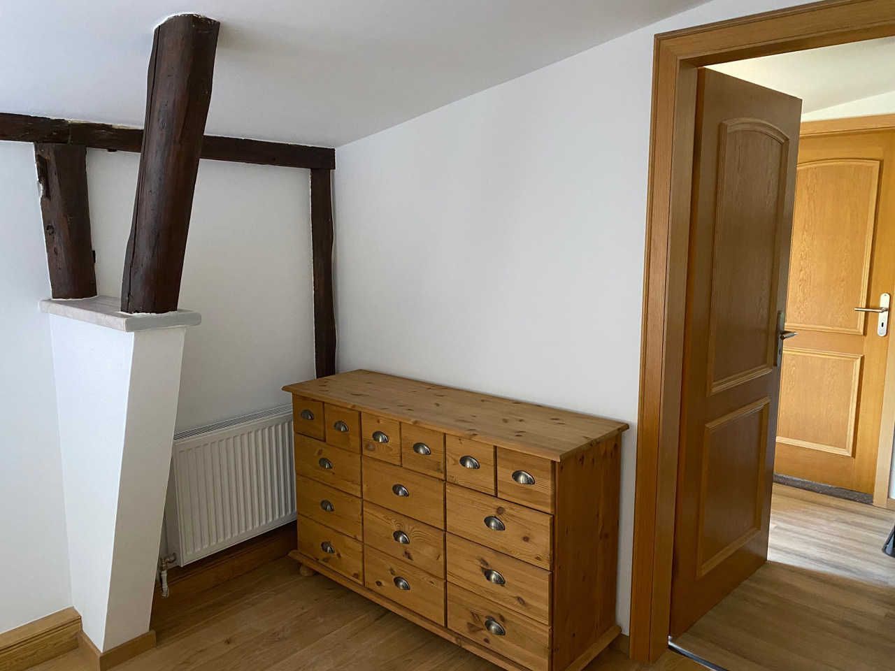 A room with a wooden dresser, a radiator, and a wooden door.