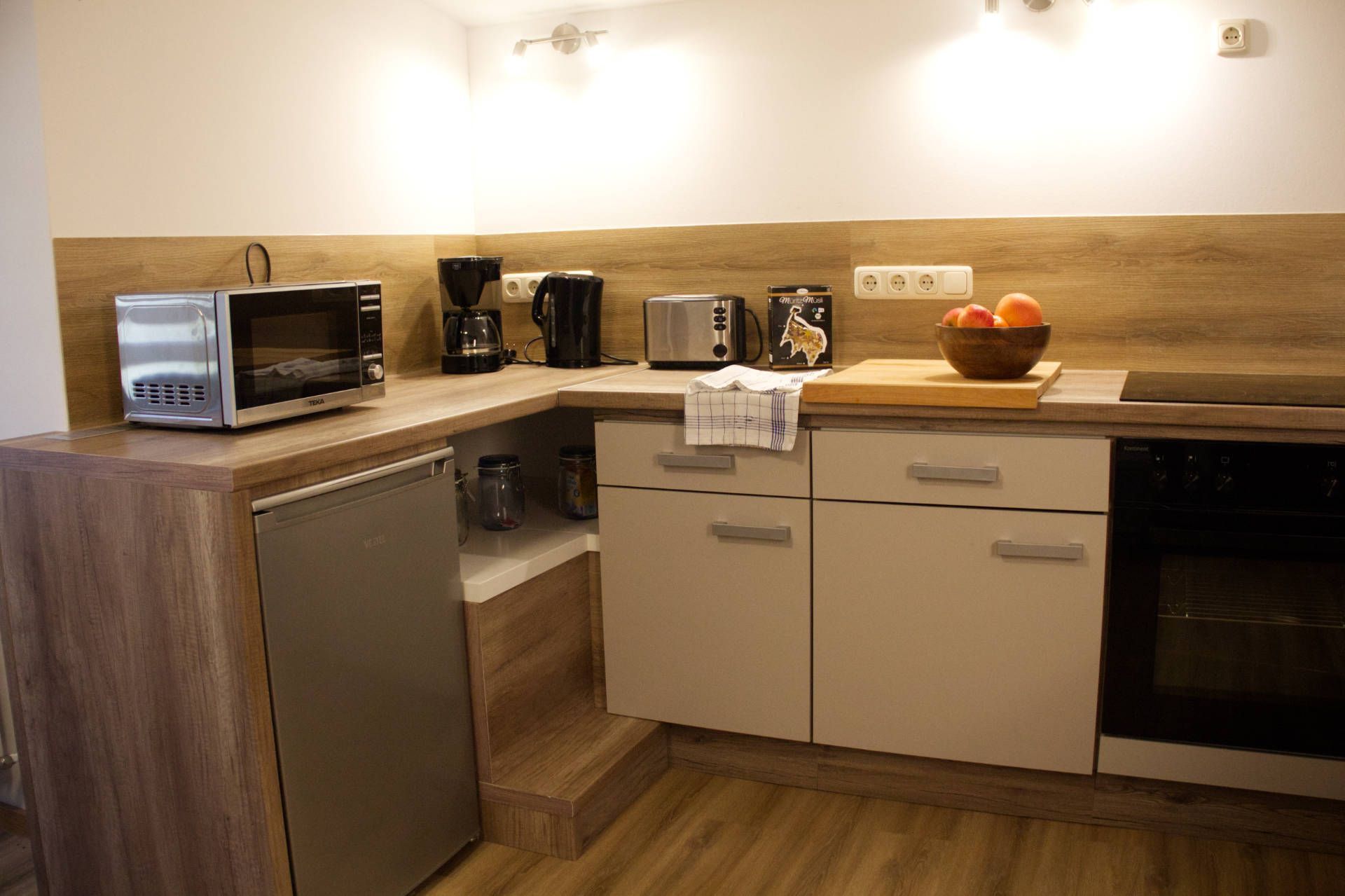 Eine kompakte Küche mit Mikrowelle, Toaster, Kaffeemaschine und einer Schüssel Obst auf der Arbeitsplatte.
