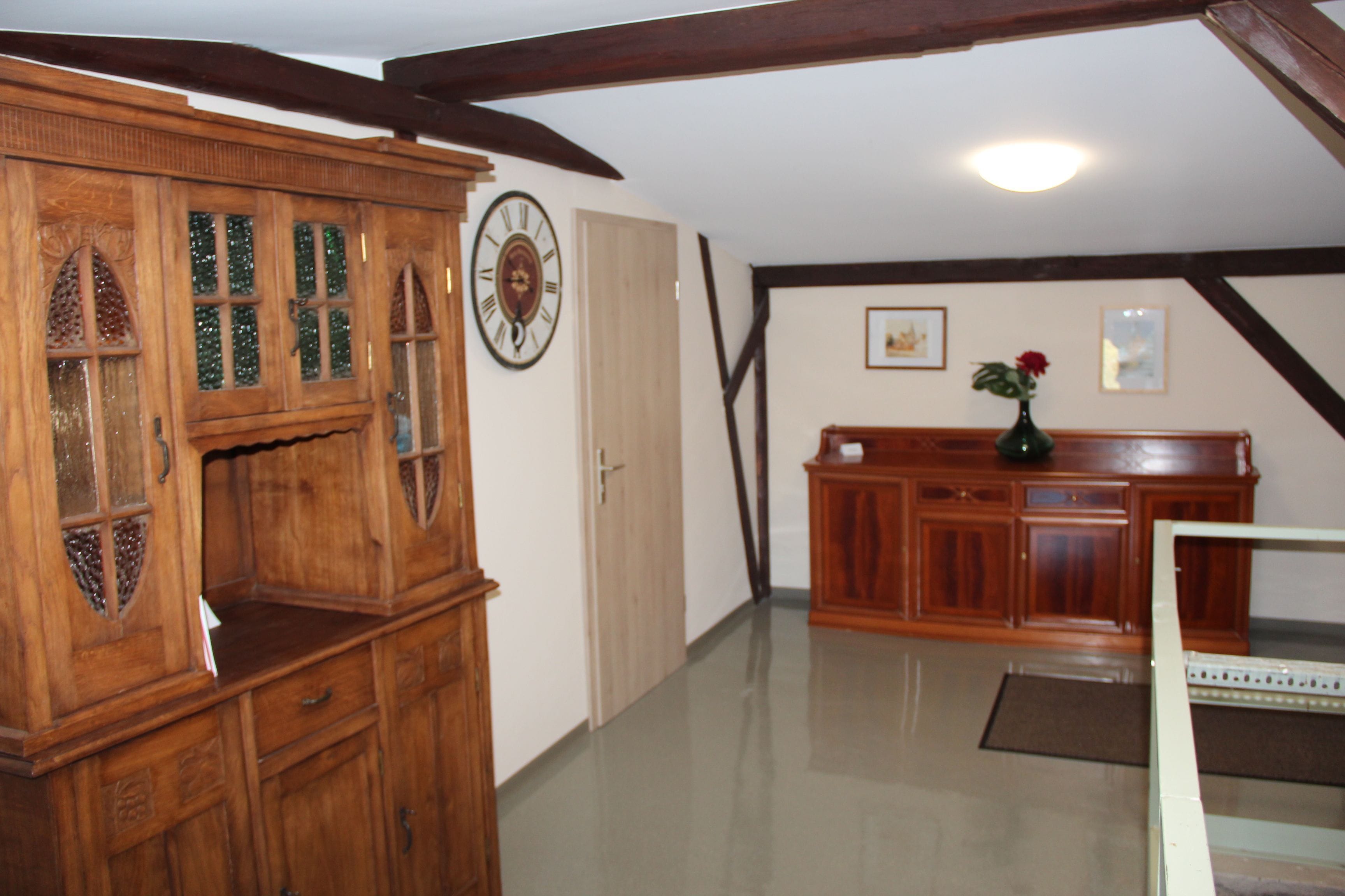 A room with wooden furniture, a clock, and a vase with flowers.