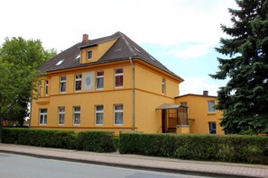 A yellow building with multiple windows, a chimney, and a small porch.