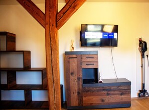 Un salon moderne avec un escalier en bois, un téléviseur fixé au mur et un aspirateur.