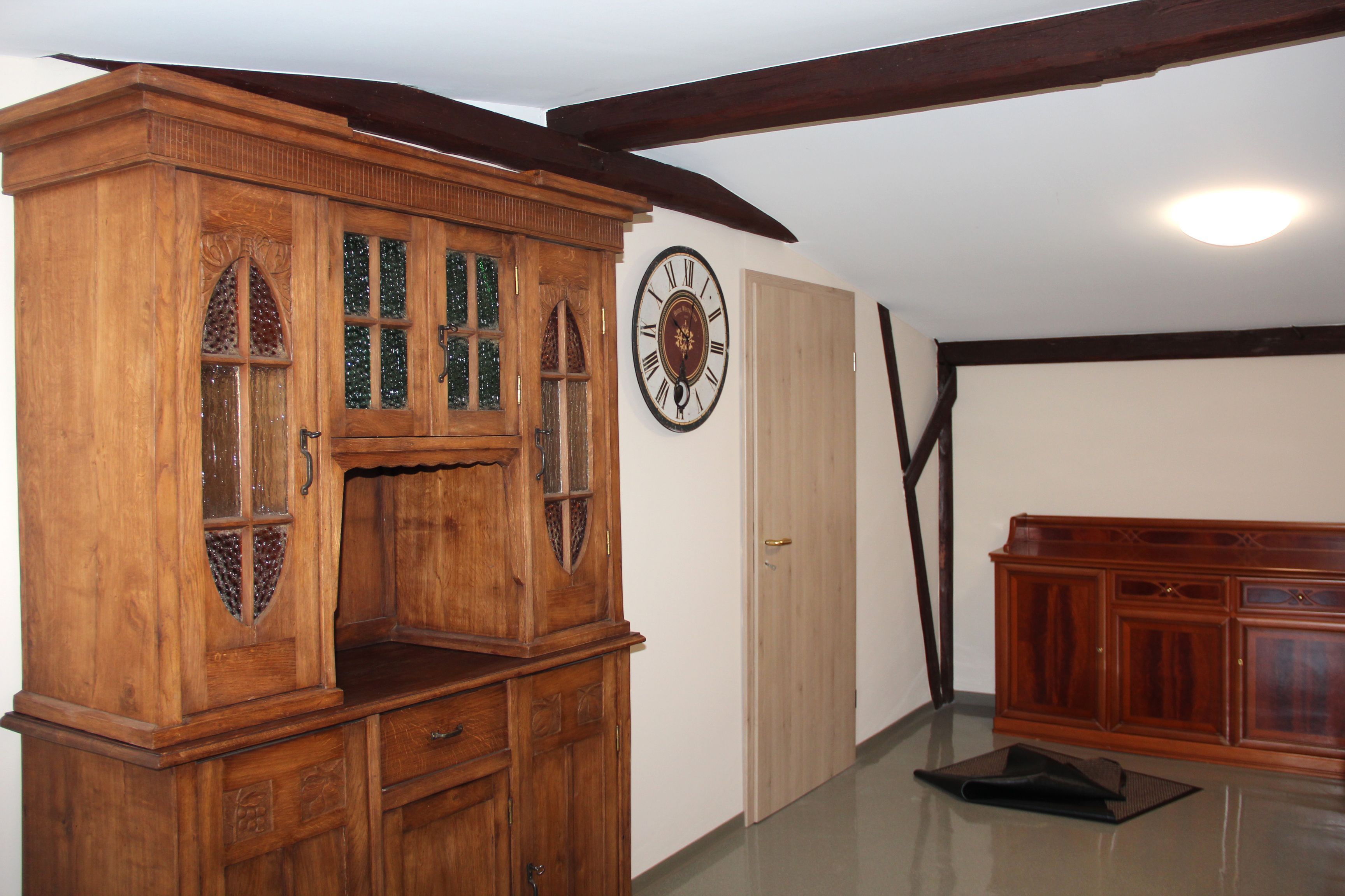 Een houten kast met glazen deuren, een wandklok en een houten bank.
