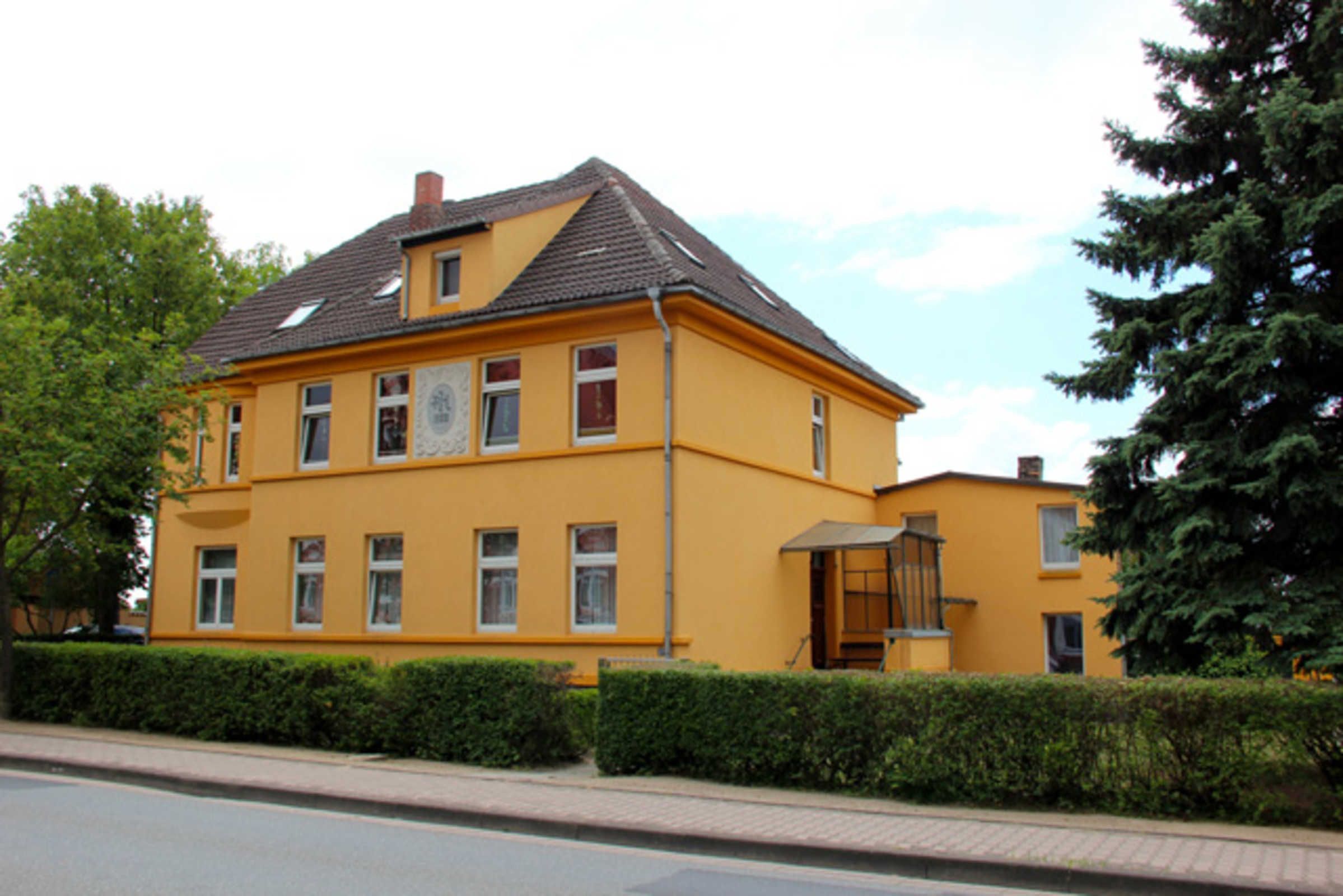 A yellow building with multiple windows, a chimney, and a small porch.