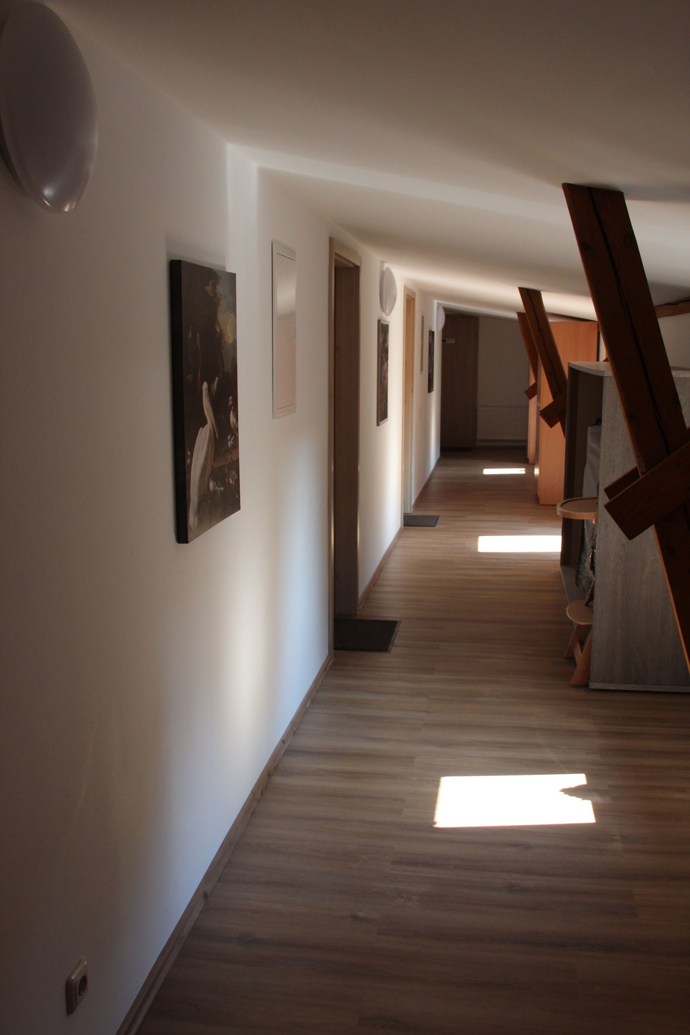 A hallway with wooden flooring, white walls, and artwork.