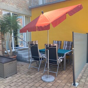Une terrasse extérieure avec une table et des chaises, un parasol rouge et une plante en pot.