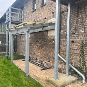 A brick building with a pergola structure, a metal fence, and a paved area. - Tenne 2 - Müritz apartment (Röbel/Müritz)