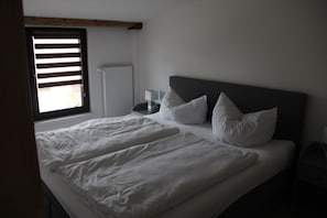 Une chambre à coucher avec un lit, des oreillers, une table de chevet et une fenêtre avec des stores.