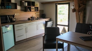 A compact kitchen with a refrigerator, microwave, and coffee maker. There is a dining area with a table and chairs. - Tenne 2 - Müritz apartment (Röbel/Müritz)