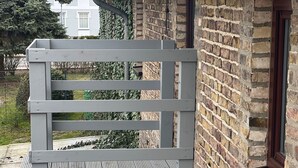 A grey bench with slatted seating and a metal backrest, positioned against a brick wall with a window. - Tenne 2 - Müritz apartment (Röbel/Müritz)