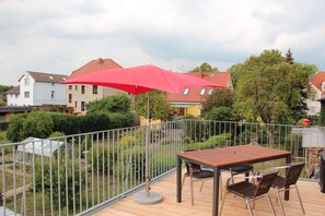 Une terrasse en bois avec une table et des chaises, un parasol rouge et une rambarde en métal.