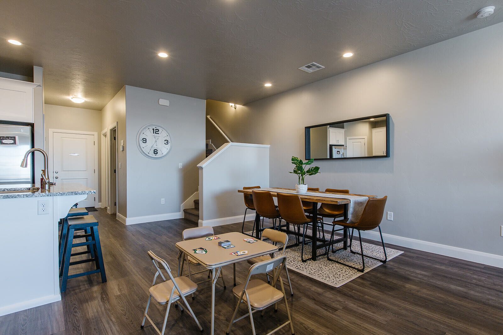 Una cocina moderna con una isla integrada, un comedor con mesa y sillas de madera, y una escalera que sube a otro nivel.