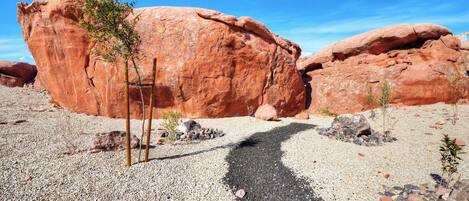 A desert landscape with large red rock formations and a gravel path leading towards them.