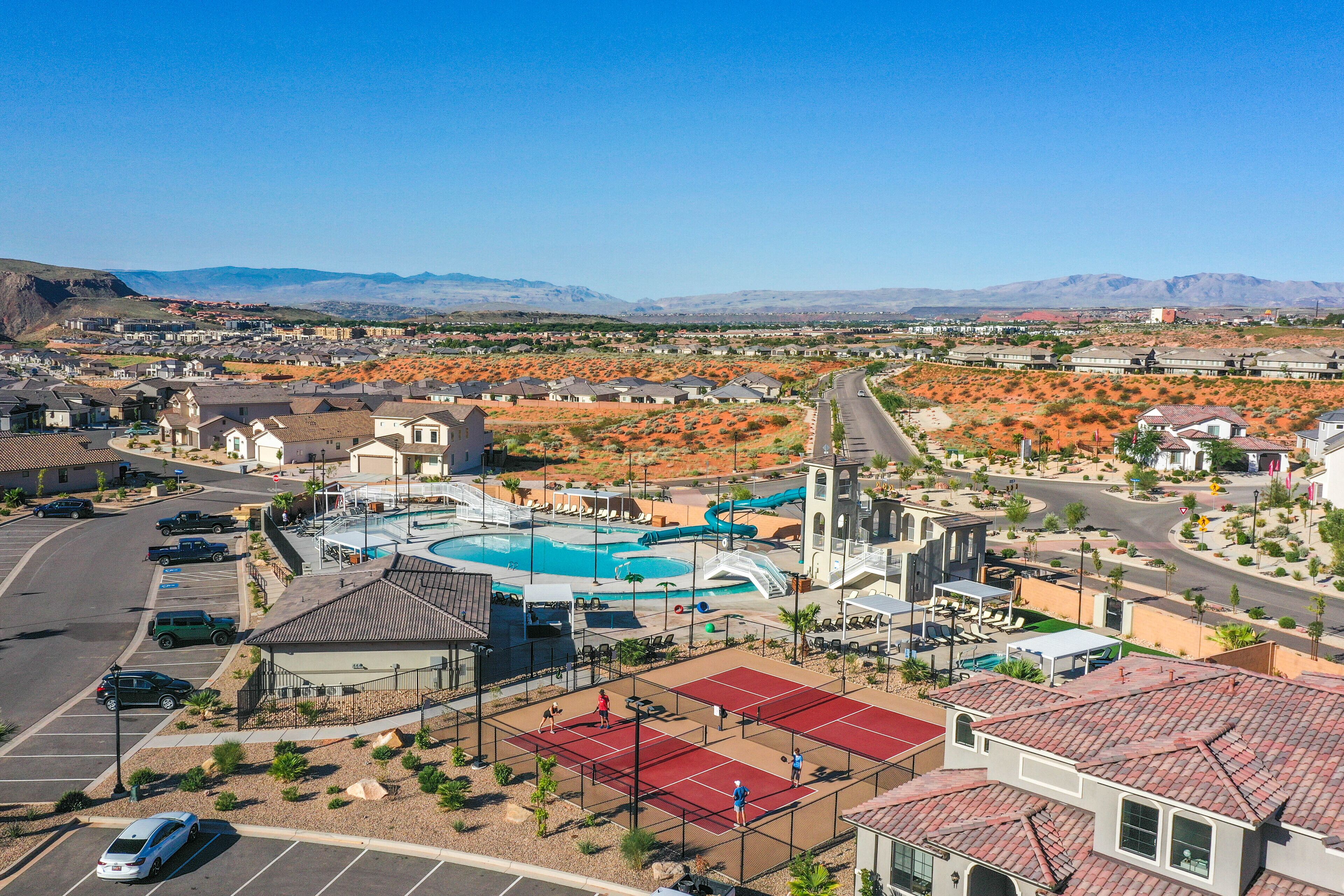 A resort with a swimming pool, tennis courts, and a desert landscape in the background.