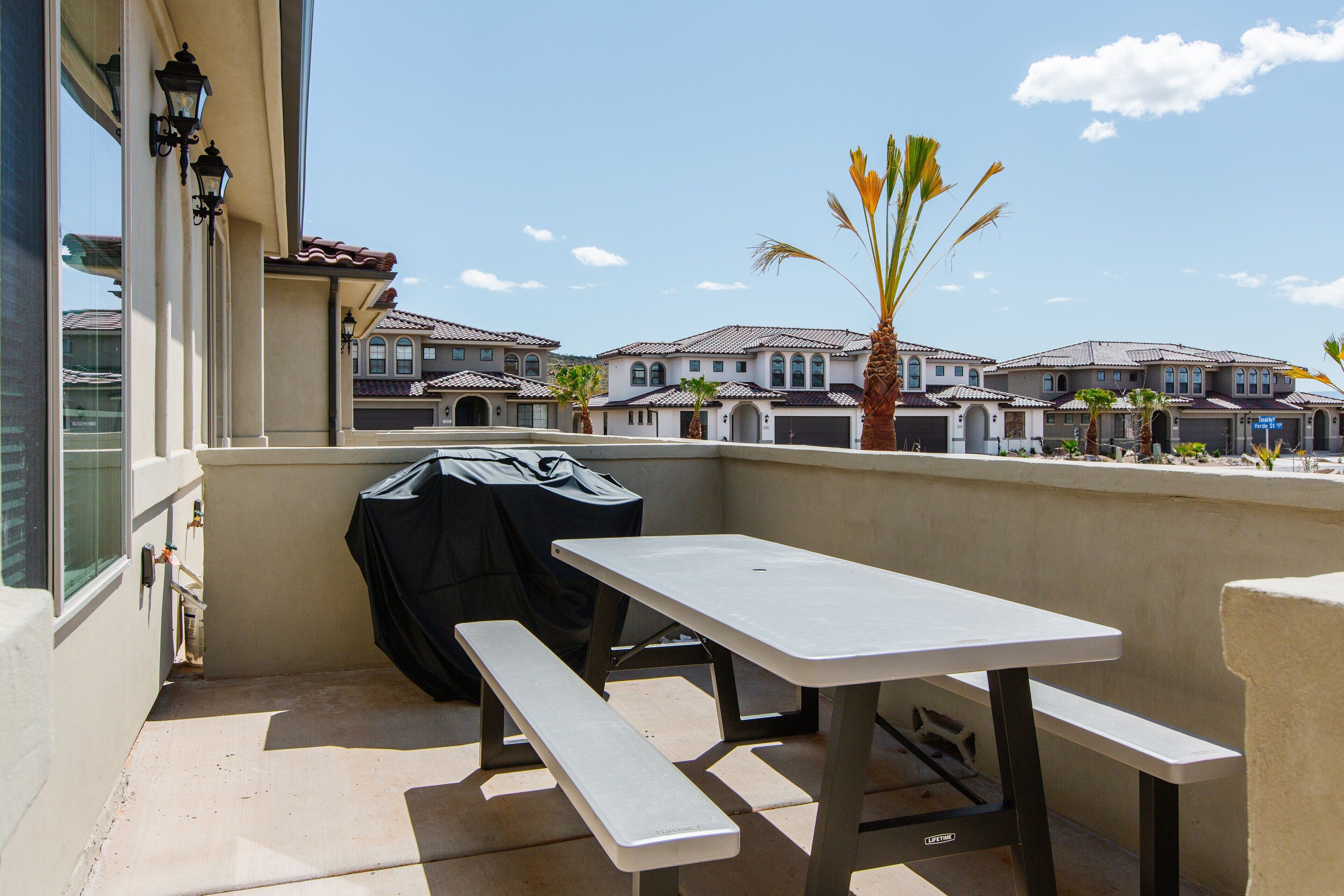 A balcony with a picnic table and grill, overlooking a row of townhouses.