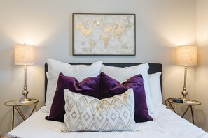 Un lit bien fait, avec une carte du monde accrochée au mur au-dessus, et de chaque côté, deux tables de chevet surmontées de lampes.