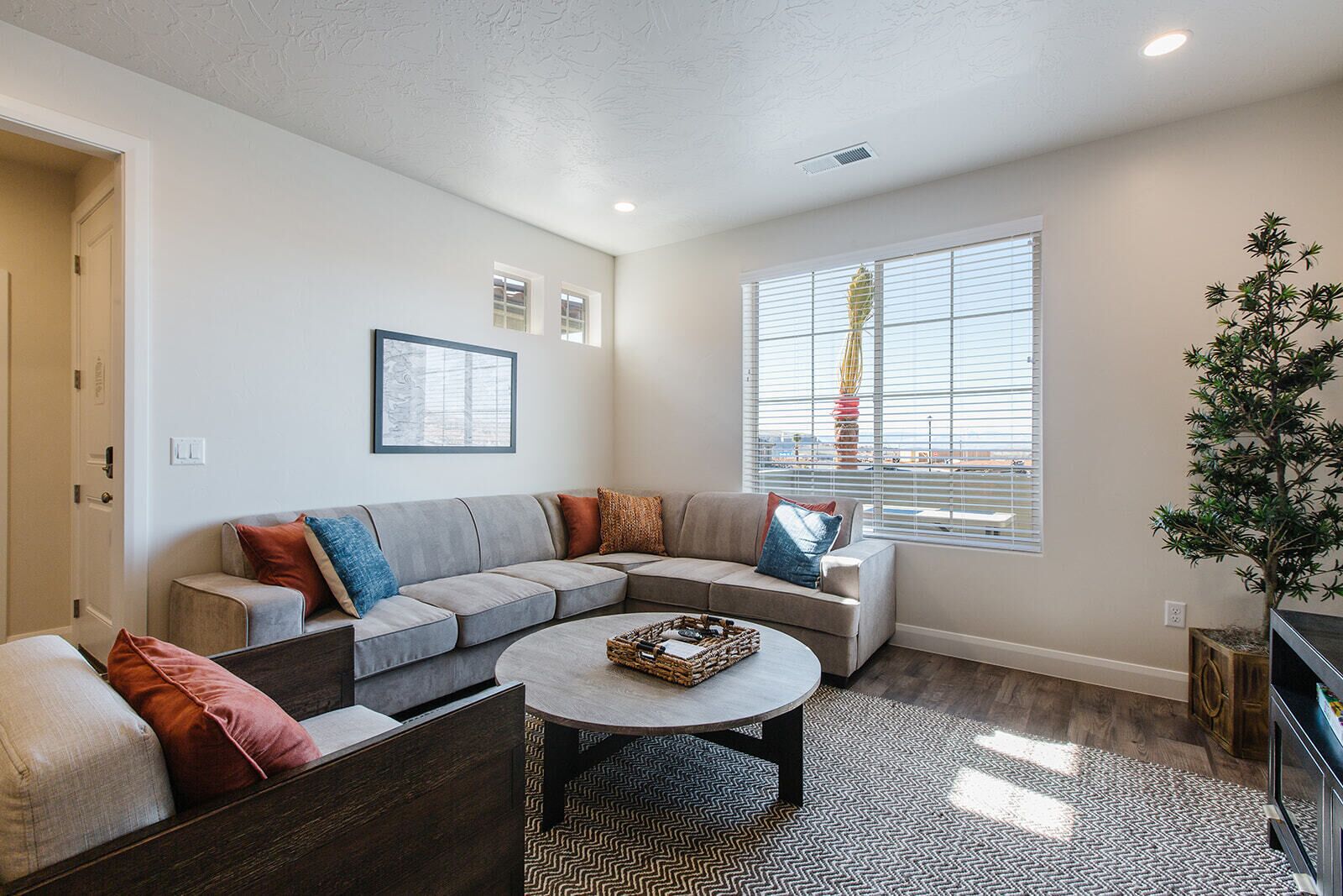 A modern living room with a sectional sofa, a coffee table, and a large window with blinds.