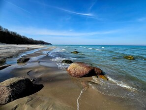 Ein Strand mit klarem, blauem Wasser, großen Felsen und einem Sandufer.