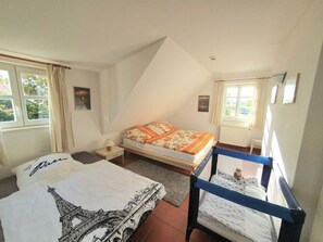 Ein Schlafzimmer mit einem Bett, einem Nachttisch, einer Kommode, einem Fenster mit Vorhängen und einem kleinen Tisch mit einer Lampe.