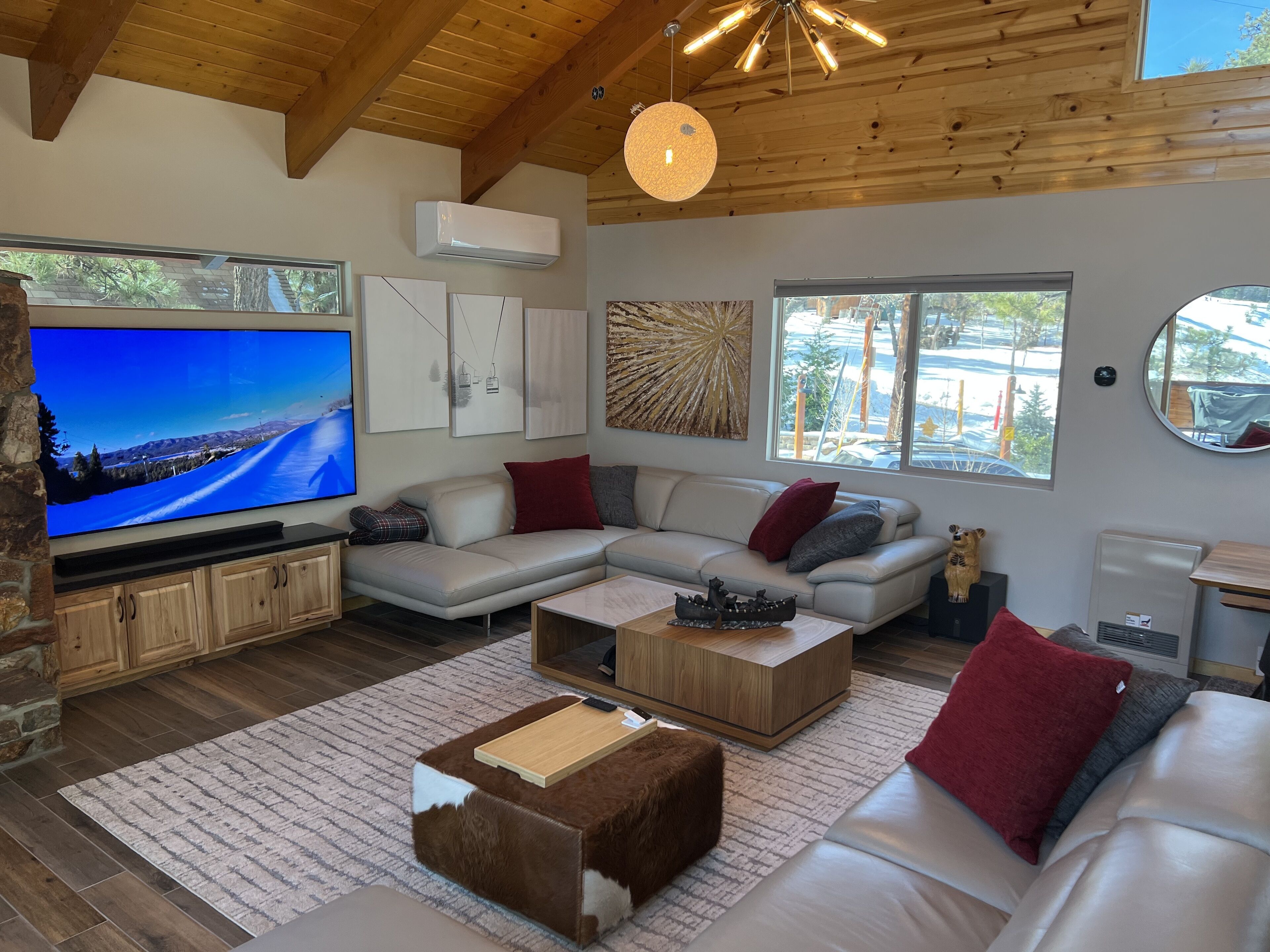 Una sala de estar moderna con un sofá seccional, un televisor de pantalla plana, pisos de madera y una pared de acento de piedra.