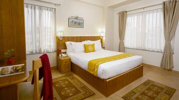 Habitación de hotel con una cama de madera, un escritorio con teléfono, una silla roja y dos alfombras decorativas.
