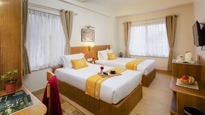 Ein Hotelzimmer mit zwei Betten, einem Schreibtisch, einem Fernseher und einem kleinen Tisch mit Obstschale.