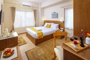 A hotel room with a bed, bedside table, and a desk with a tray of wine glasses and a bottle. - Pema Boutique Hotel (Kathmandu)