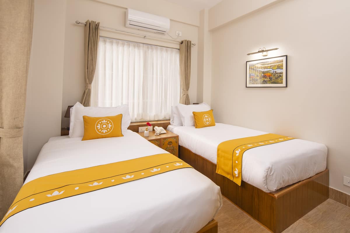A hotel room with two beds, a nightstand with a phone, and a wall-mounted air conditioner.