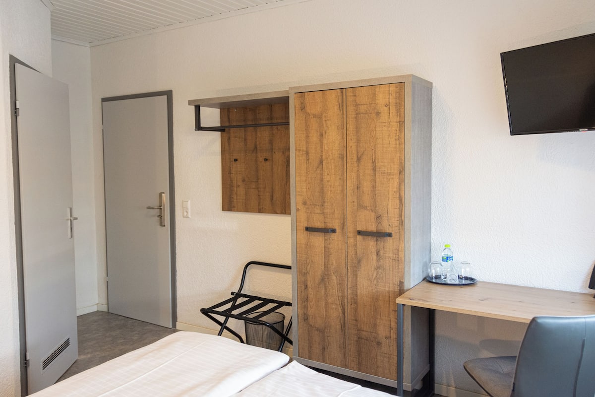 Una habitación de hotel con cama, un armario de madera, un escritorio con silla y televisión montada en la pared.