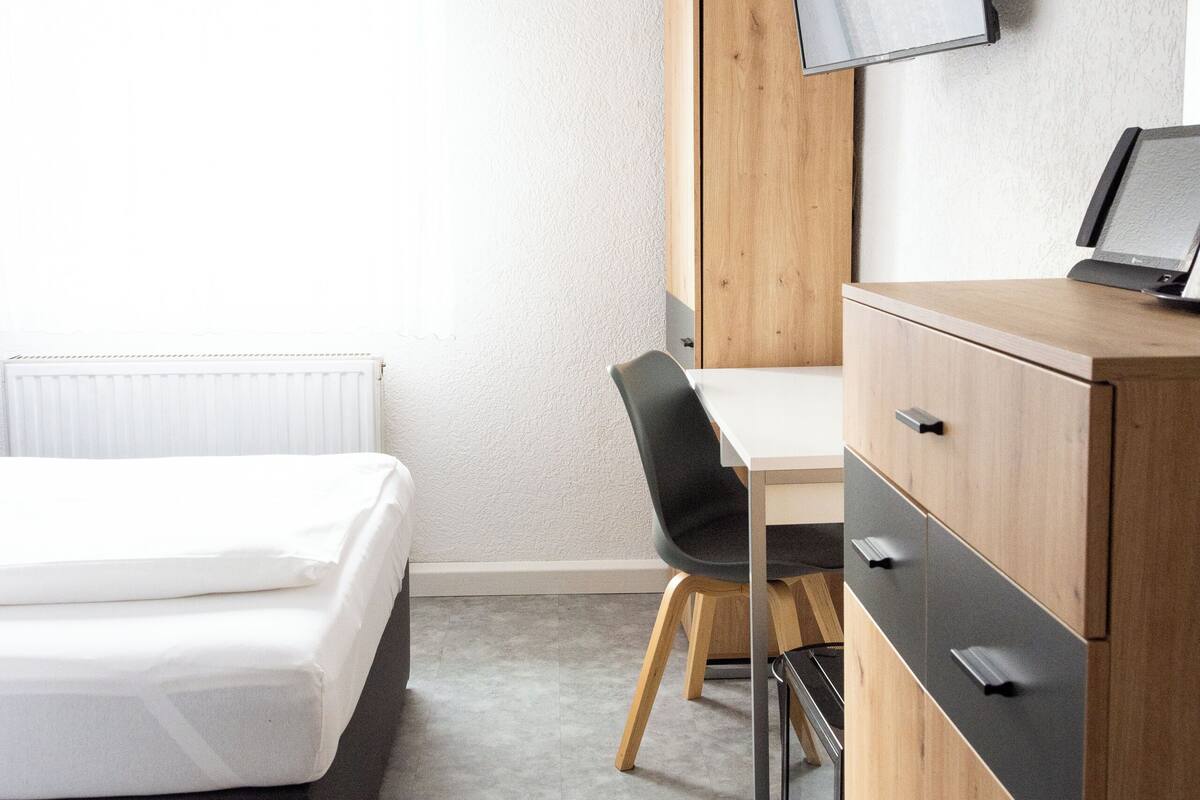 Un dormitorio moderno con una cama, un escritorio, una silla, un televisor y un armario.