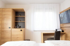 Hotellihuone, jossa on puinen vaatekaappi, työpöytä tuolilla, sänky ja suuri ikkuna, jossa on läpikuultavat verhot.