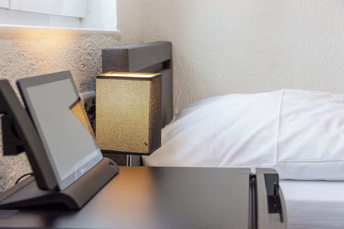 Una habitación moderna con una cama, una mesita de noche con un ordenador portátil y una lámpara de pared.