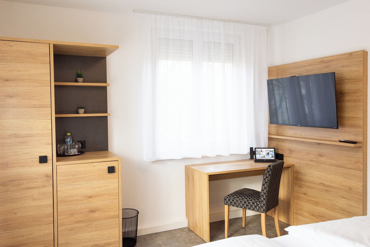 Habitación de hotel con escritorio de madera, una silla, televisor montado en la pared y armario con estantes.