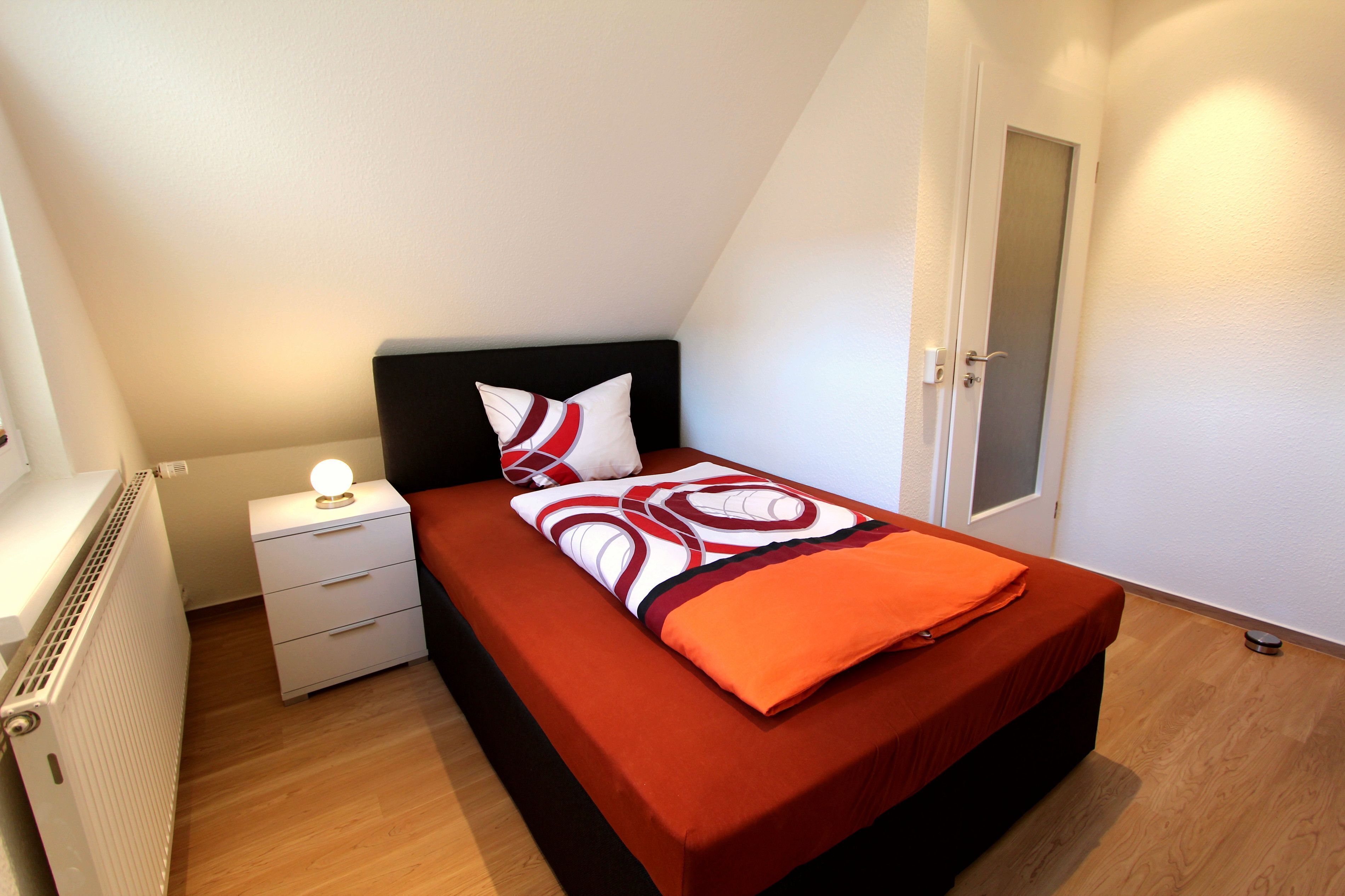 Una camera da letto con un letto, un comodino, un termosifone e una porta.