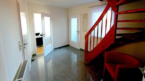 Un couloir avec un escalier rouge, des portes blanches et un radiateur.