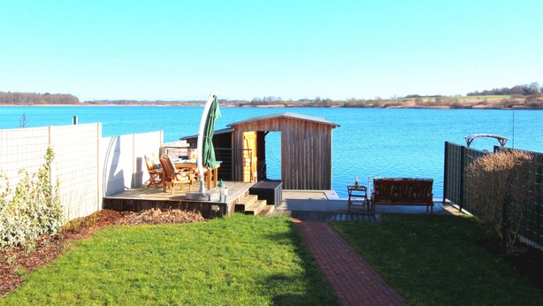 Une terrasse au bord du lac, dotée de sièges extérieurs, une petite construction en bois et une vue dégagée sur le lac.