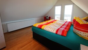 Une chambre à coucher avec un lit, un radiateur, une fenêtre et un balcon.