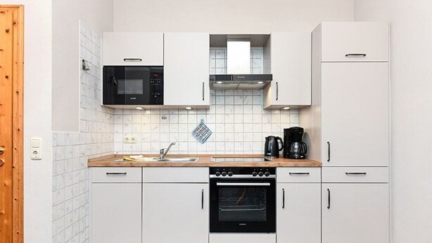 A modern kitchen with white cabinets, a microwave, a coffee maker, and an oven. - Apartment West - Ferienhof Deich in sight (Esens)