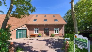 A brick building with a tiled roof, a green door, and a sign that reads "Deich in Sicht Ferienwohnung Familie Peters." - Apartment West - Ferienhof Deich in sight (Esens)