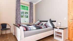 A bedroom with a bed, a chair, a nightstand, and a window with curtains. - Apartment West - Ferienhof Deich in sight (Esens)