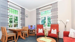 A room with a dining table, two red armchairs, a sofa, a TV, and a clock on the wall. - Apartment West - Ferienhof Deich in sight (Esens)