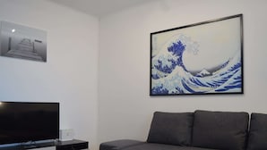Una sala de estar moderna con un televisor de pantalla plana, una mesa de centro, un sofá y una obra de arte enmarcada que representa una ola.