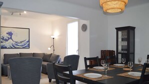 Un comedor con una mesa negra dispuesta para cuatro personas, rodeada de sillas oscuras. Se observan una lámpara moderna y un reloj en las paredes.
