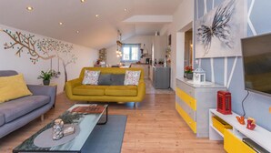 A modern living room with a sofa, coffee table, and a TV. There is a kitchen in the background with a dining area. - Pet friendly home in Tinj (Tinj)