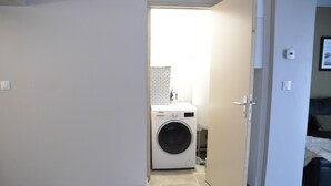 A laundry room with a washing machine and dryer, a tiled floor, and a door leading to a bedroom.